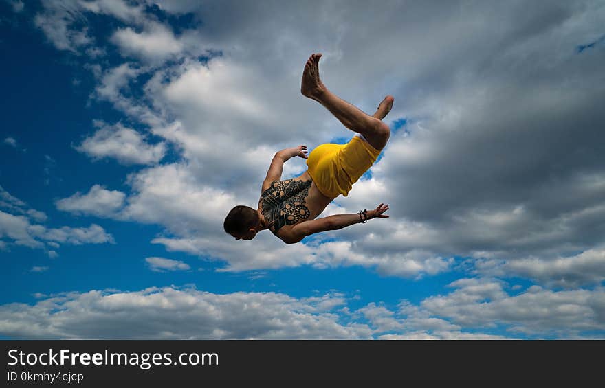 Tricking on street. Martial arts. Man performs jump with flip-flop barefoot. Shooted from bottom foreshortening against sky. Tricking on street. Martial arts. Man performs jump with flip-flop barefoot. Shooted from bottom foreshortening against sky.