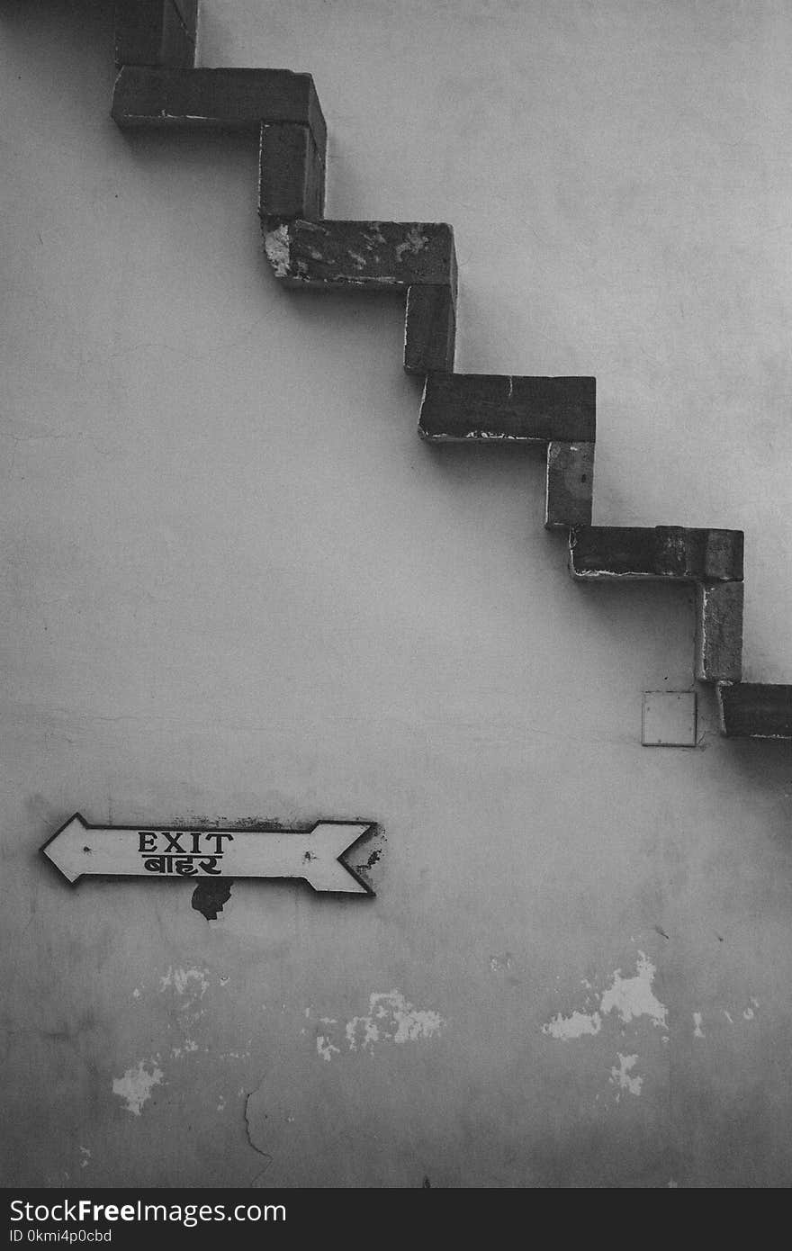 Grayscale Photo of Exit Signage Under Brown Stairs