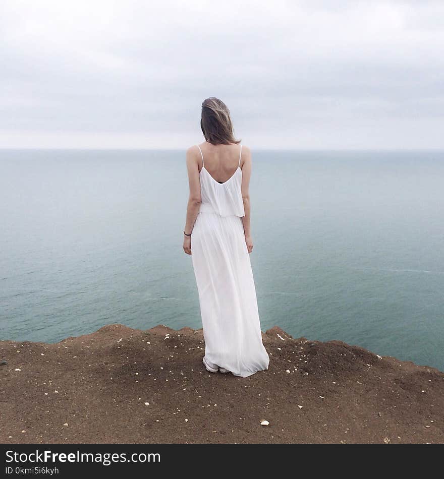 Woman in White Spaghetti Strap Dress Standing on Cliff