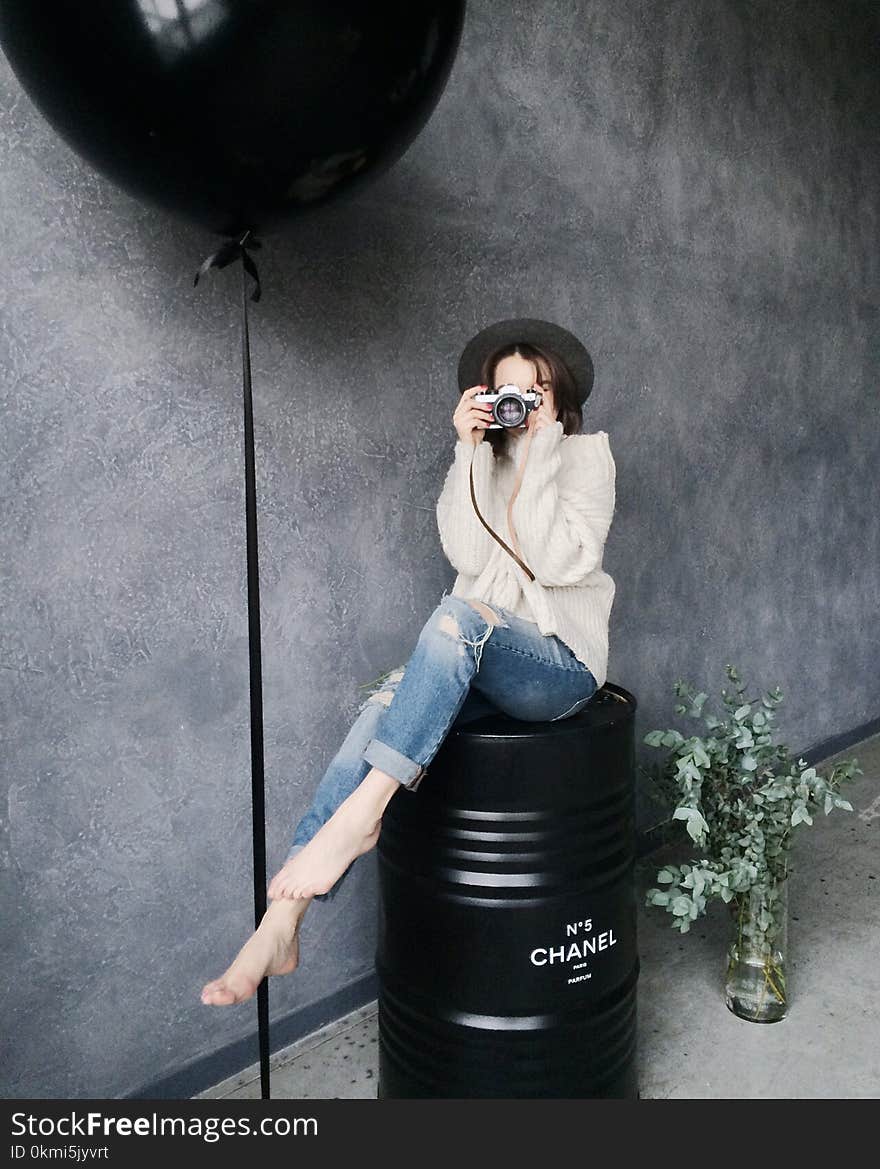 Woman Using Silver Camera Sitting on Black Container Drum