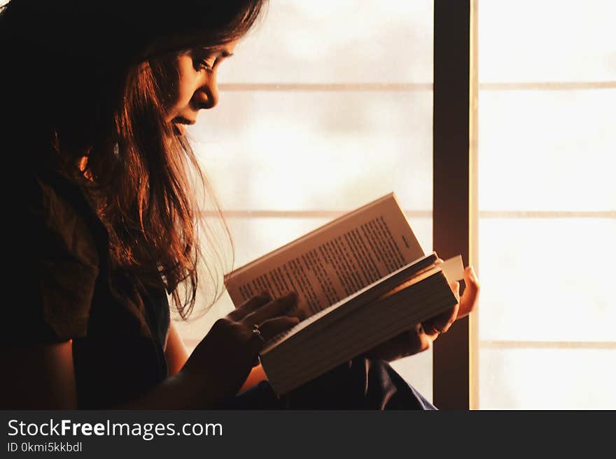 Woman Reading a Book Beside the Window