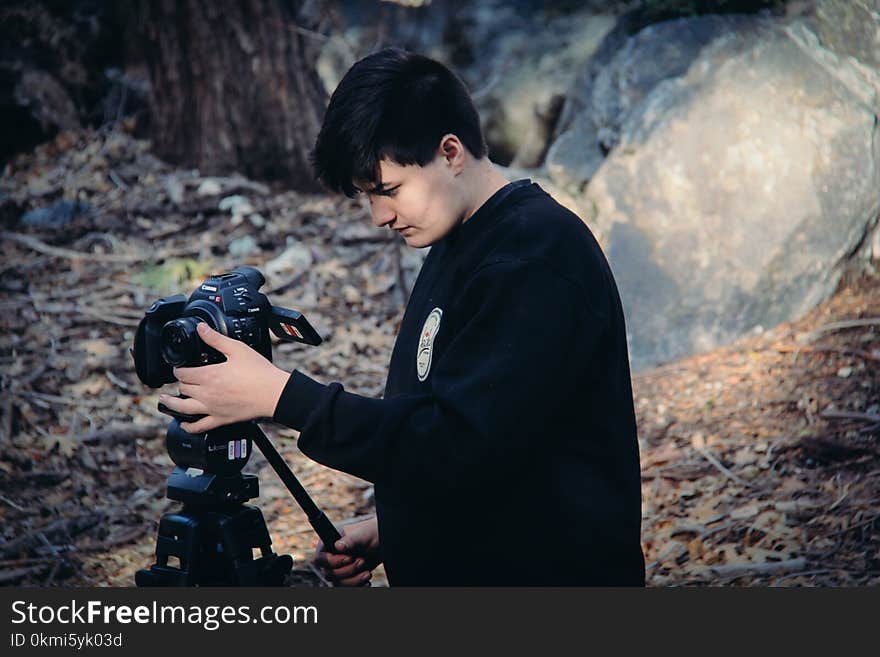 Man Holding and Looking at Dslr Camera on Camera Stand