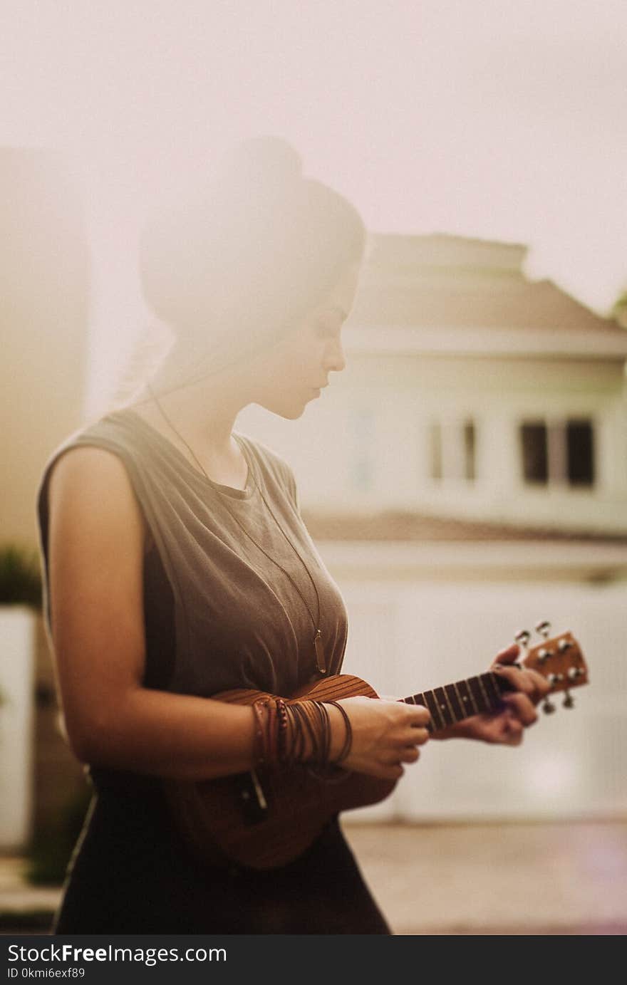 Woman in Brown Sleeveless Dress While Playing Ukulele