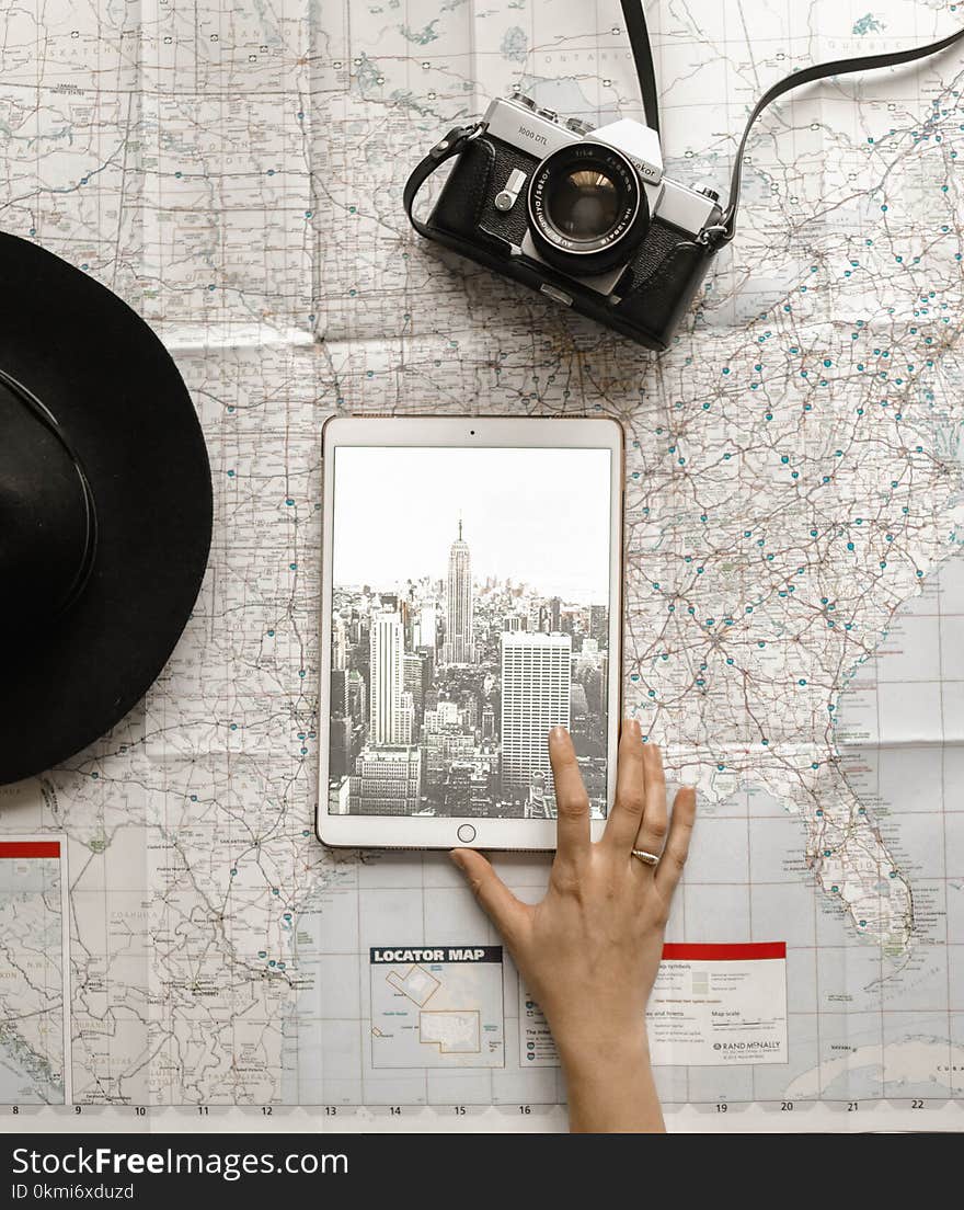 Flat Lay Photography of Person Touching Silver Ipad on World Map Chart Beside Black Hat