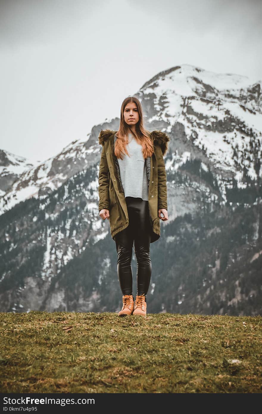 Woman Wearing Green Jacket in Front of Snowy Mountain