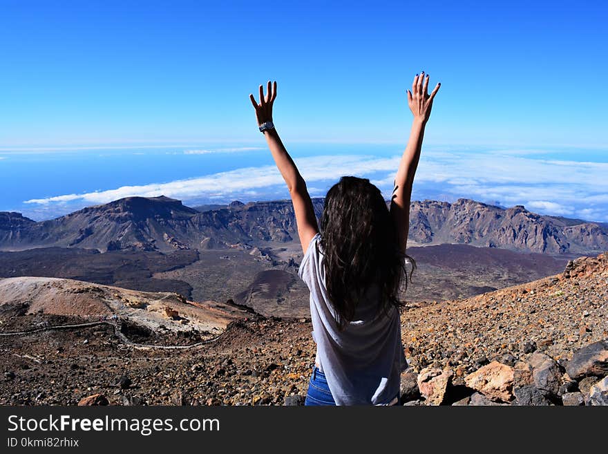 Woman Standing on Mountain While Raising Her Hands