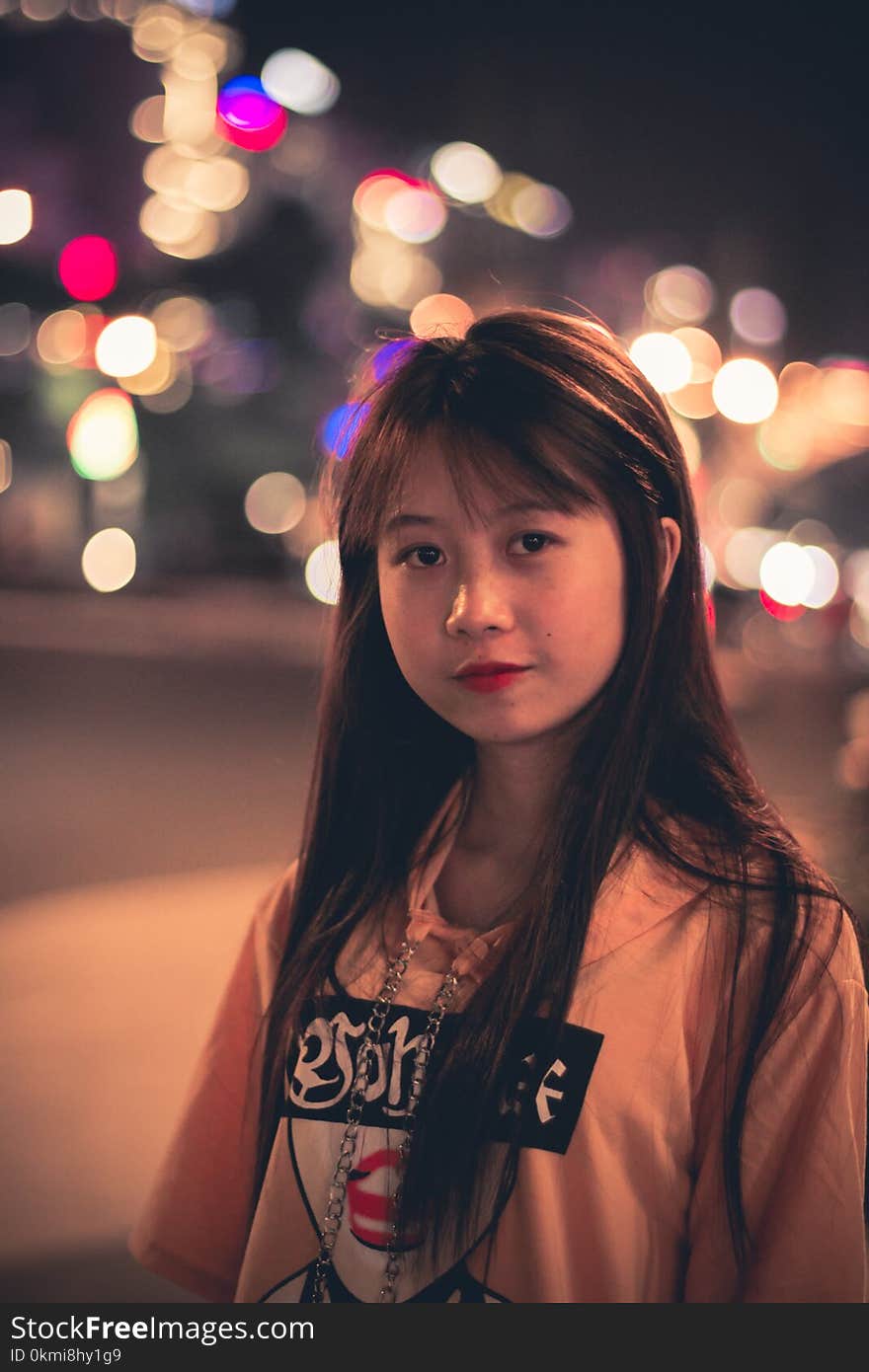 Woman Wearing Pink, Black, and Red Printed Pullover Hoodie Standing Beside Road Bokeh Photography at Night Time