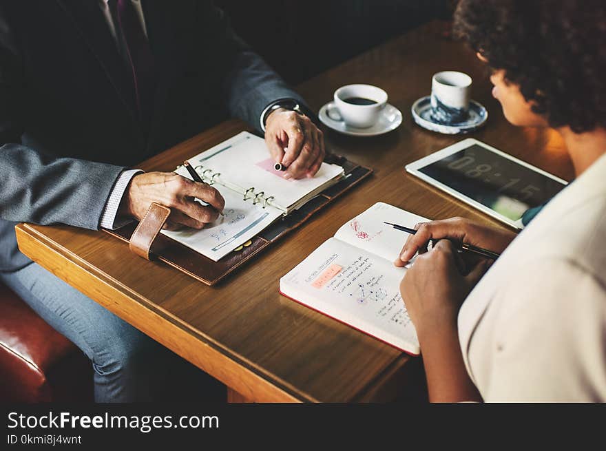 Man and Woman Sitting in Front of Table With Books and Cup of Coffee Facing Each Other