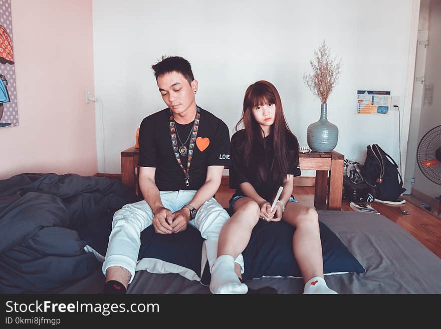 Man and Woman Wearing Black Shirts Sitting on Bed