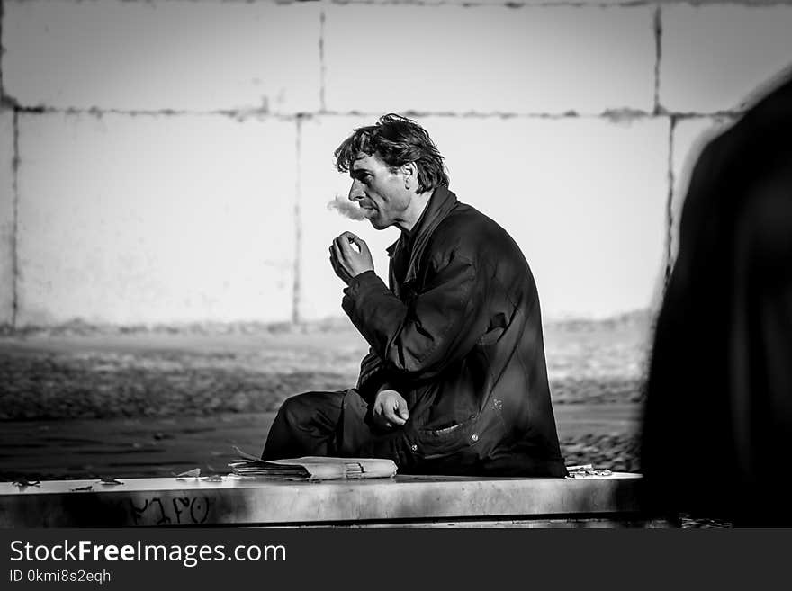 Grayscale Photo of Smoking Man While Sitting on Bench