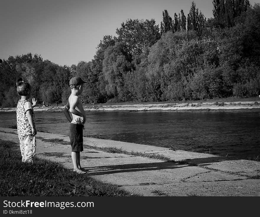 Grayscale Photo of Oy Boy and Girl Standing Near Body of Water