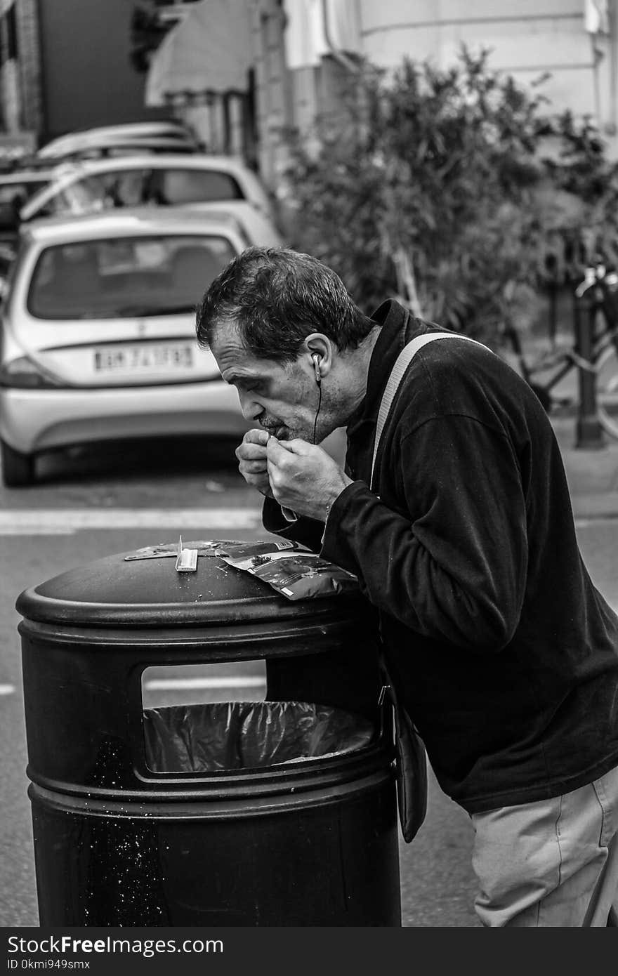 Grayscale Photography of Man Leaning on Black Trash Bin