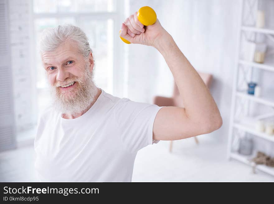 Upbeat senior man raising hand while holding dumbbell