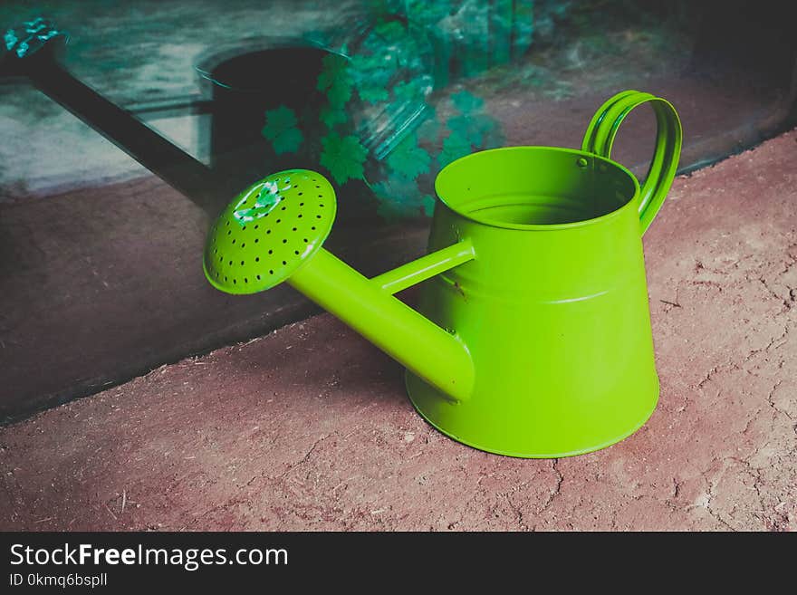 Watering can on the garden close up shoot. Photo depicts bright colorful green watering can standing alone. Happy and cheerful gardening care concept.