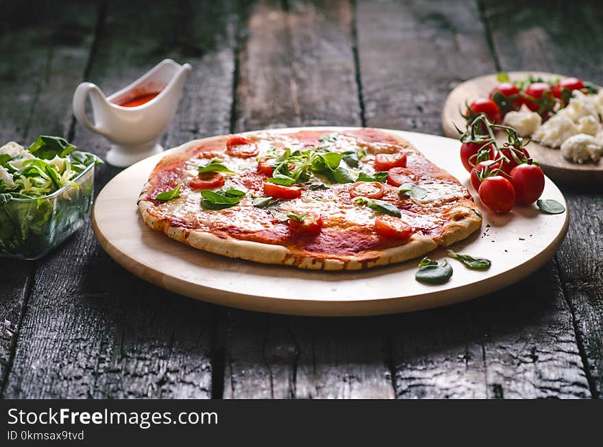 Italian food, cuisine. Margherita pizza on a black, wooden table with igredients like tomatoes, salad, cheese, mozzarella, basil.