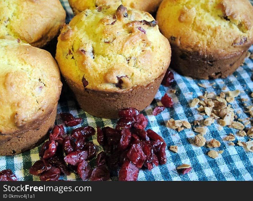 Freshly baked cranberry oatmeal muffins closeup with loosely scattered oats and dried cranberries on a blue-green gingham cloth background. Freshly baked cranberry oatmeal muffins closeup with loosely scattered oats and dried cranberries on a blue-green gingham cloth background