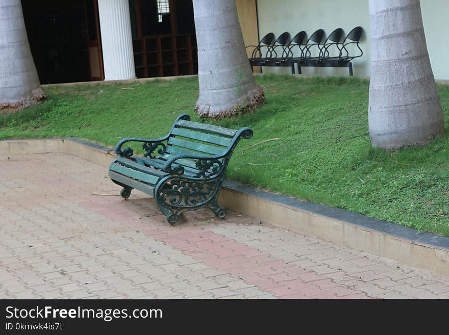 Green Metal Bench Beside Concrete Curb and Green Grass