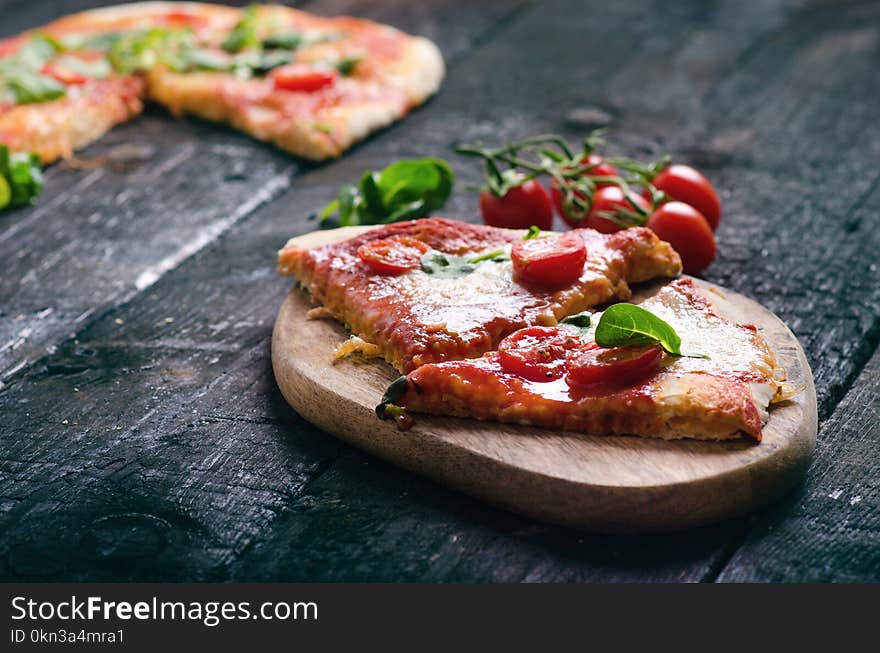 Italian food, cuisine. Margherita pizza on a black, wooden table with igredients like tomatoes, salad, cheese, mozzarella, basil.