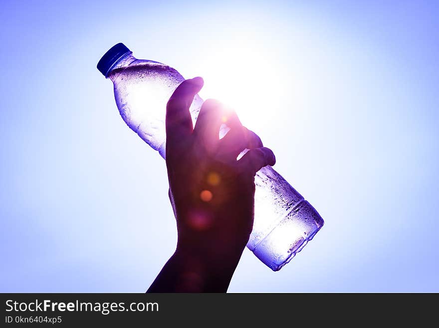 Silhouette of closeup Woman`s hand holding plastic water bottle over sunlight effect. World Water Day concept.