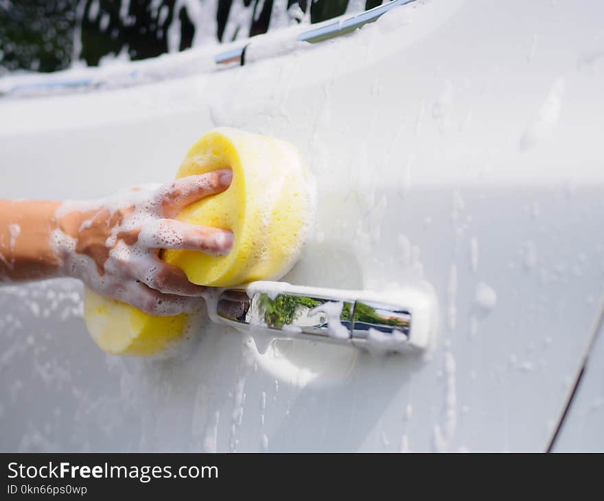 Woman hand with yellow sponge washing car