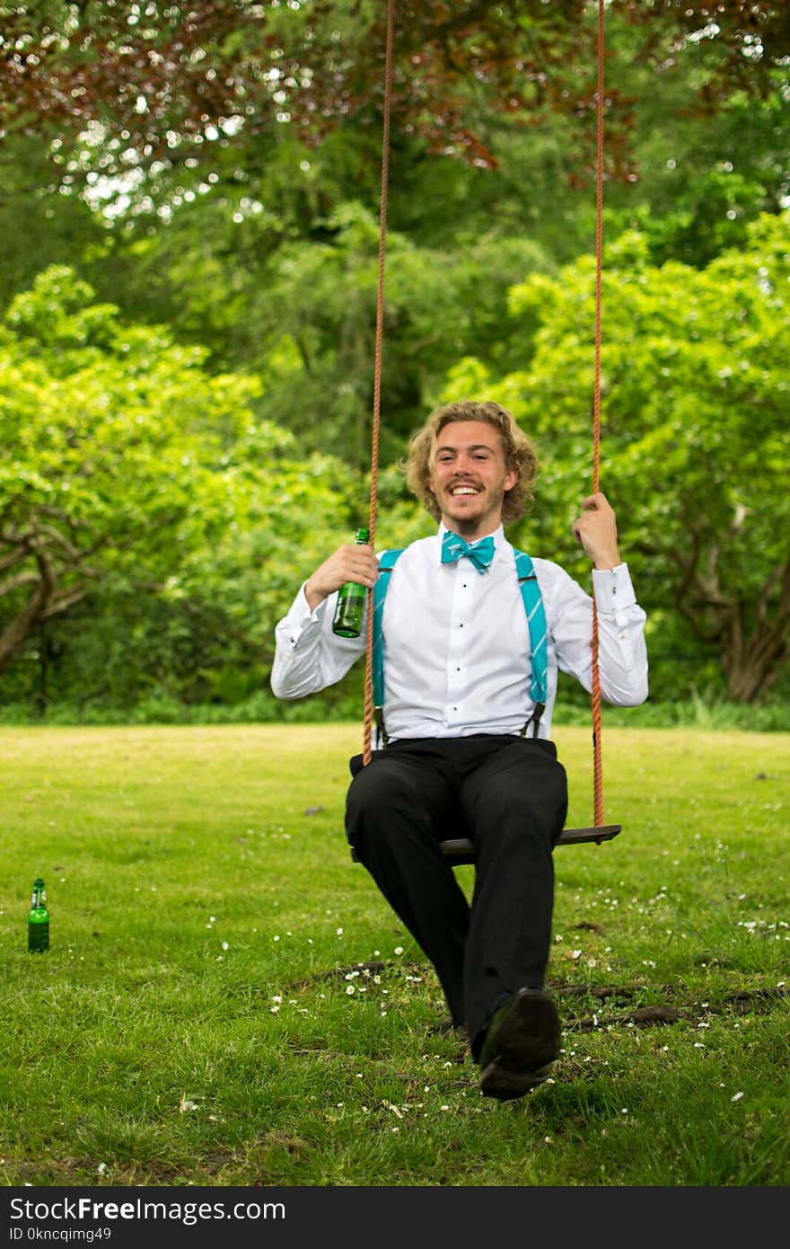 Man in White Dress Shirt and Black Pants Sitting on Swing