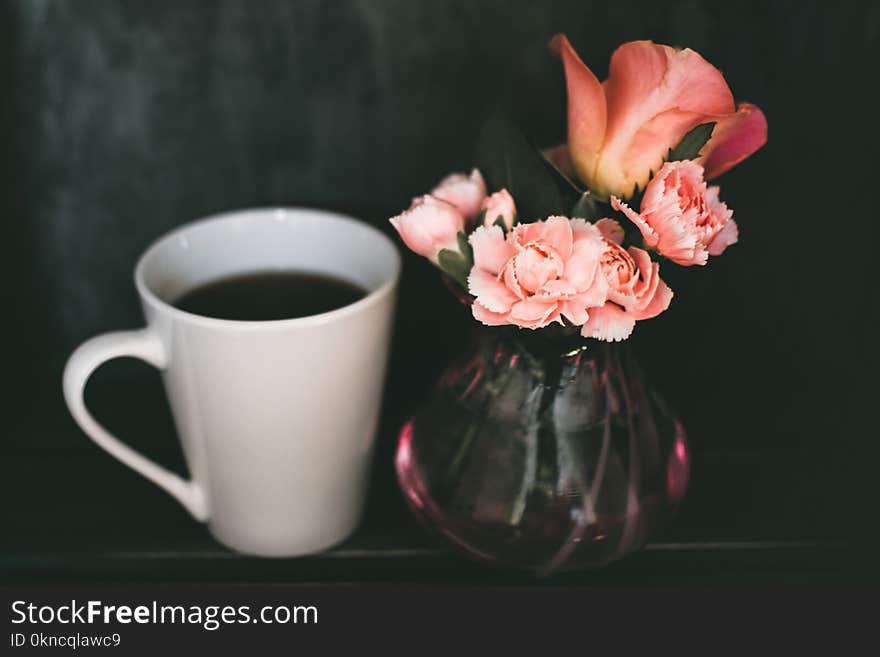 Pink Carnation Flower and Pink Rose Flower in Clear Glass Vase Beside Mug of Coffee