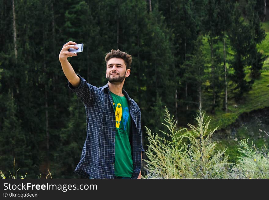 Man in Blue Sports Shirt and Green Top Taking a Selfie Near Green Trees