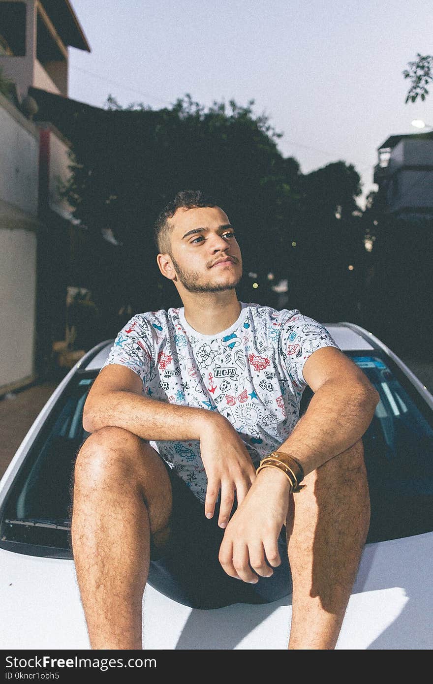 Man in White and Blue Crew-neck T-shirt Sitting on Top of White Car