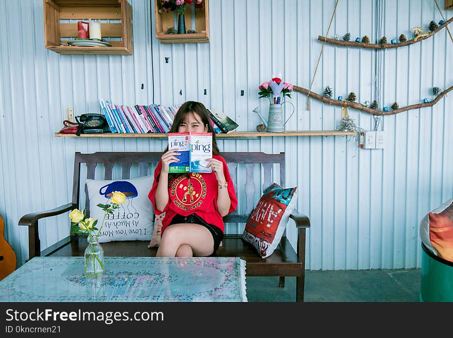 Woman in Red Shirt Holding Book Sitting on Bench in Front of Coffee Table