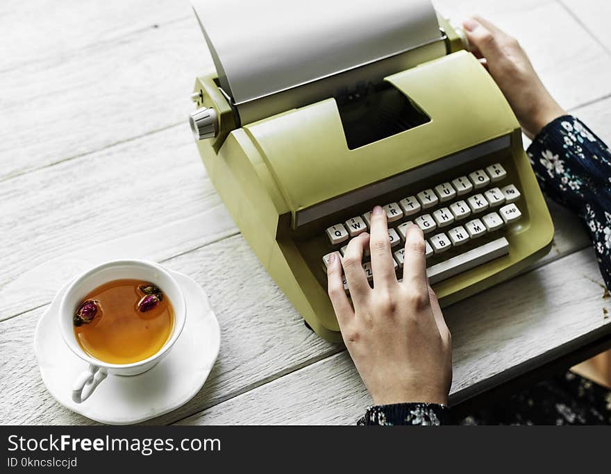 Person Holding Type Writer Beside Teacup and Saucer on Table