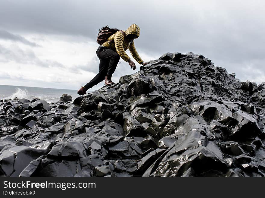 Man Wearing Hoodie and Black Pants Climbing Up Pile of Rocks