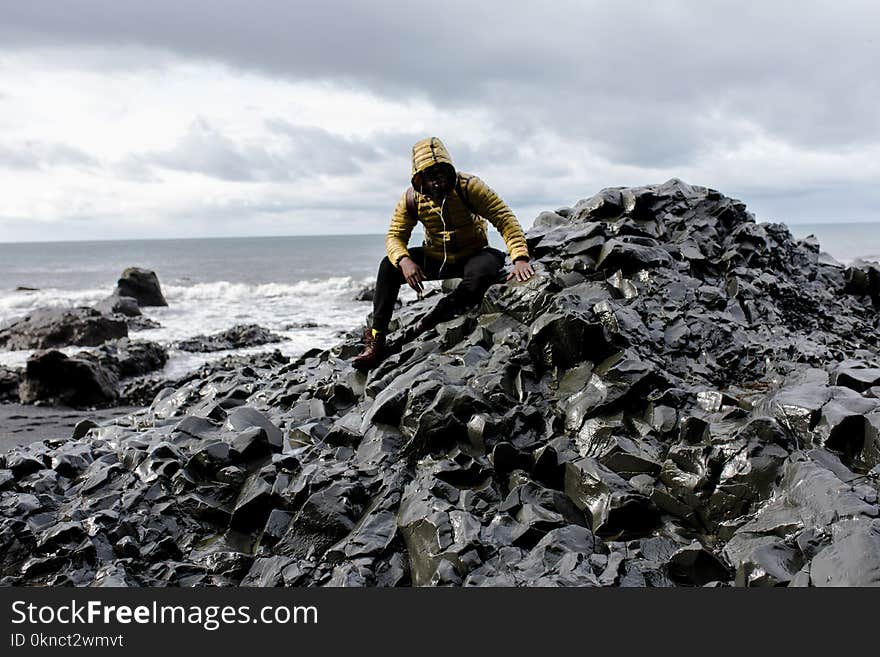 Selective Color Photography of Man Wearing Hoodie on Stone Behind Body of Water