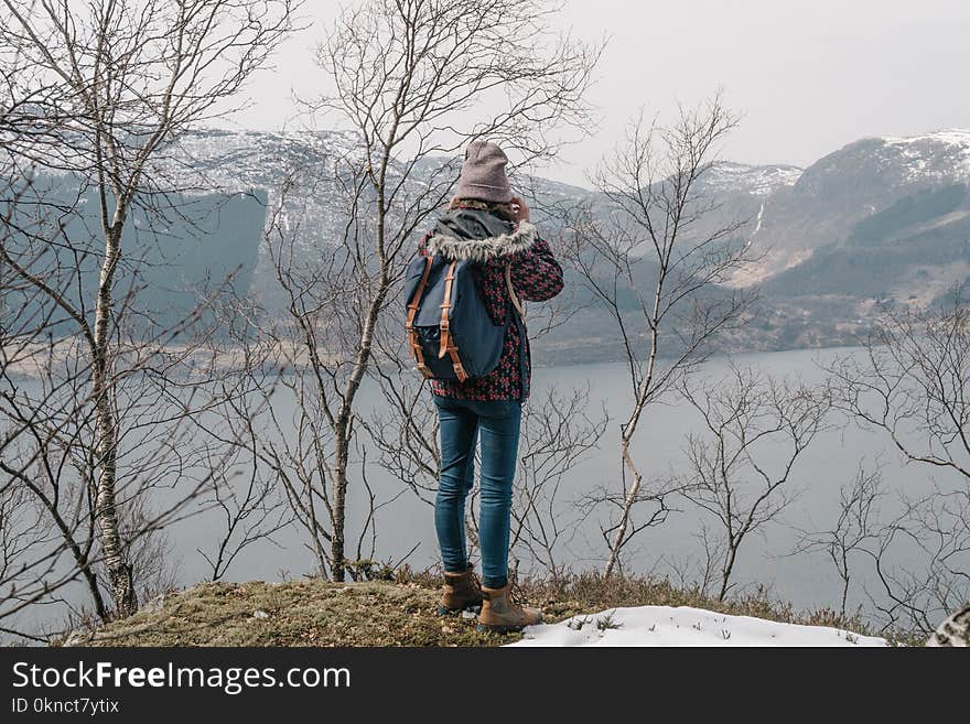 Woman in Brown Coat and Blue Jeans Near the Lake