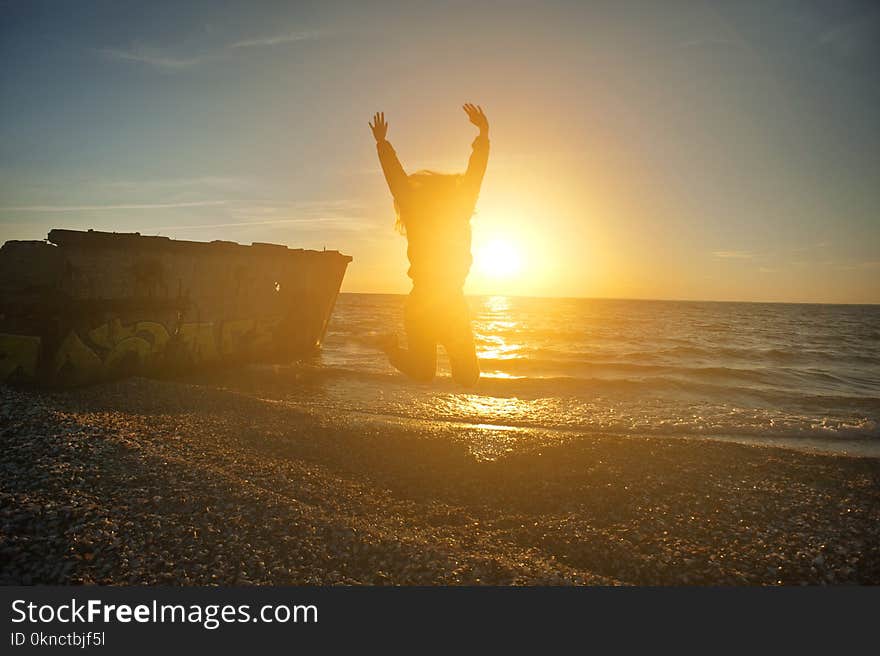 Person Jumping on Seashore during Golden Hour