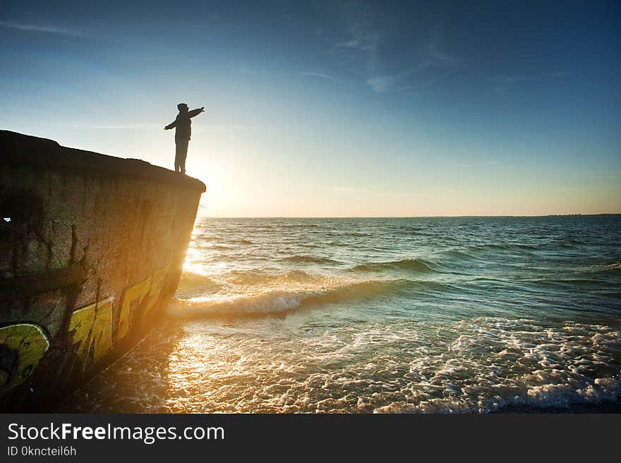 Silhouette of Person on Cliff Beside Body of Water during Golden Hour