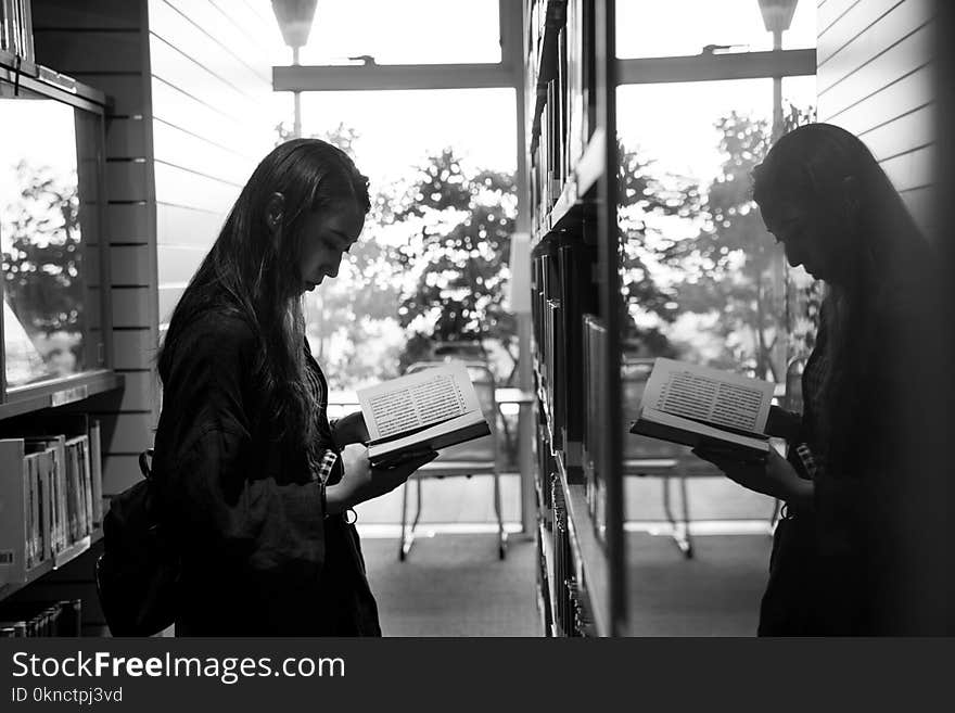 Greyscale Photo of Girl Reading a Book Reflecting on a Glass