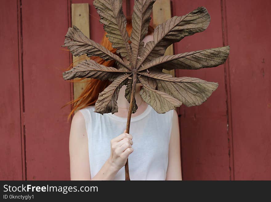 Woman in White Sleeveless Shirt Gold Brown Leaf in Front of Her Face