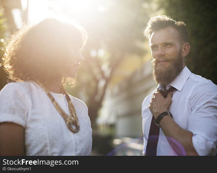 Man Holding His Necktie While Looking at Woman Wearing White Top