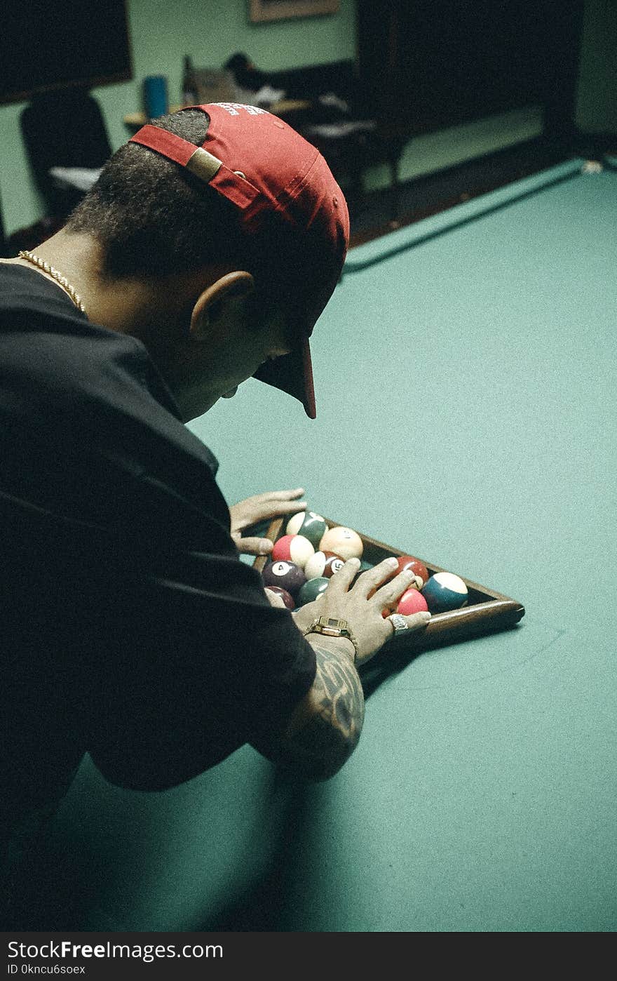 Man in Black T-shirt and Red Baseball Cap Arranging Billiard Balls on Table