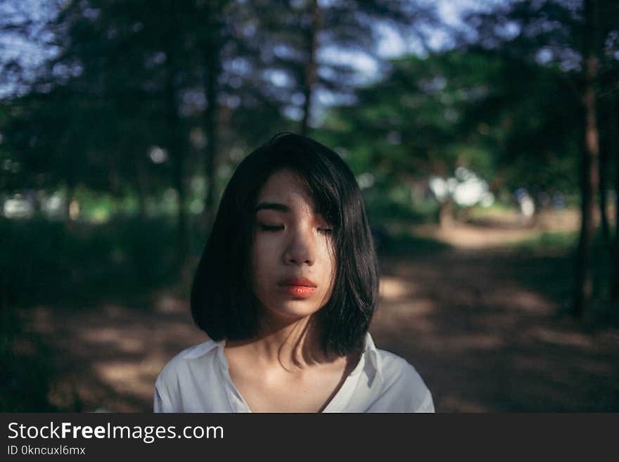 Shallow Focus Photography of Woman in White Top Beside Green Trees