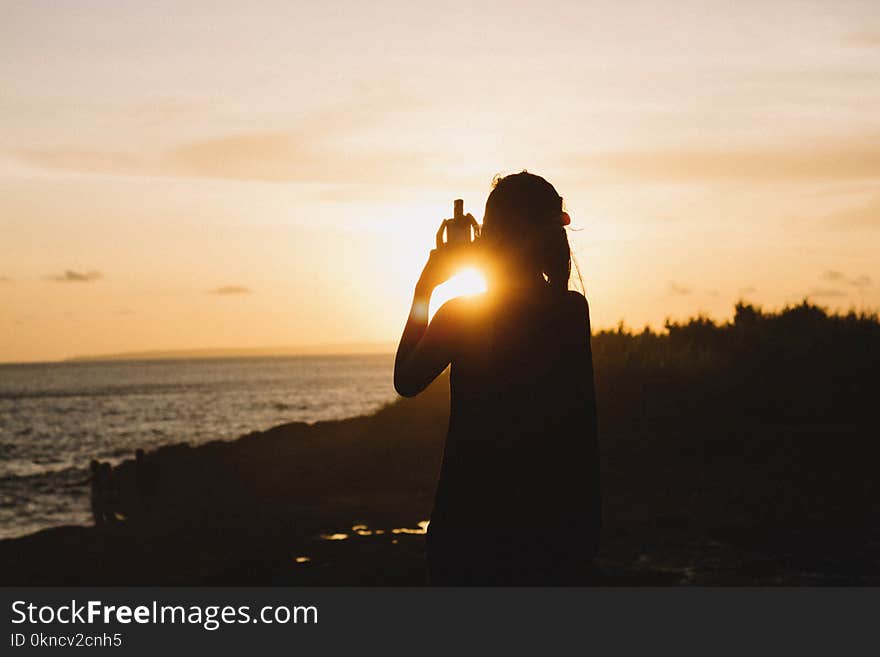 Silhouette of Woman Standing Near Body of Water during Sunset