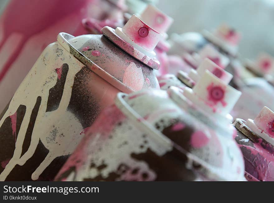 A lot of dirty and used aerosol cans of bright pink paint. Macro photograph with shallow depth of field. Selective focus on the spray nozzle