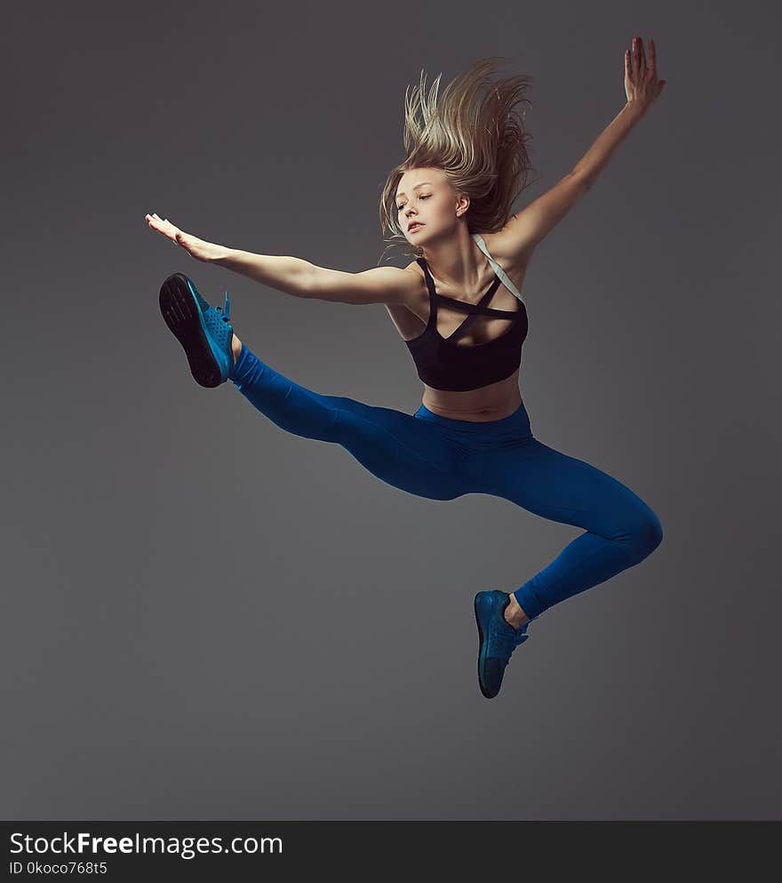 Young blonde ballerina in sportswear dances and jumps in a studio. Isolated on a gray background.