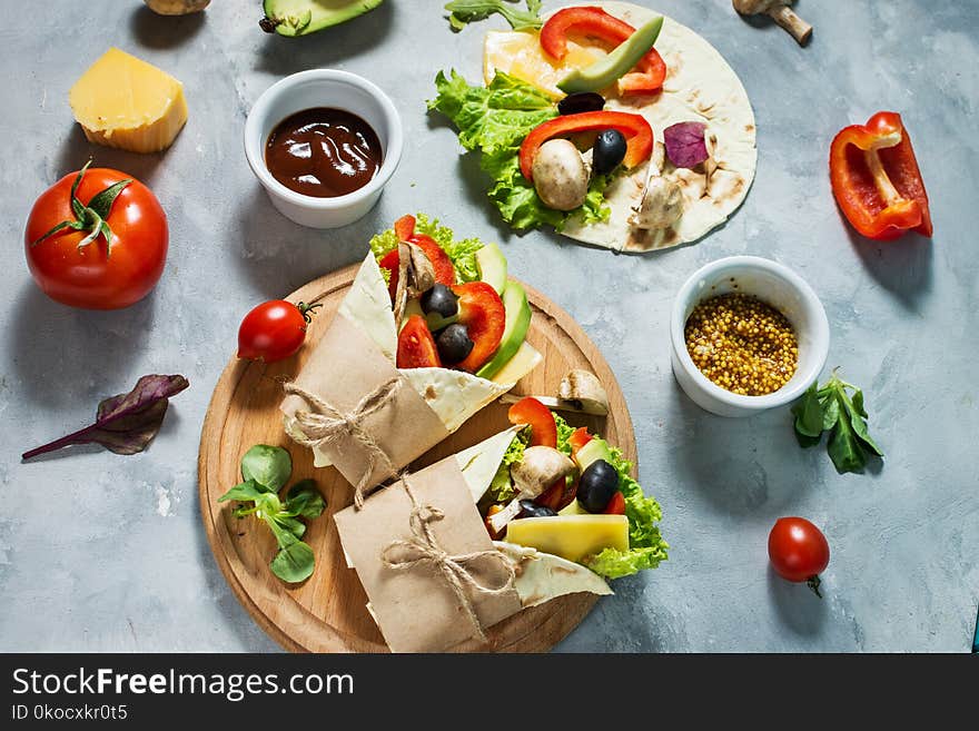 Healthy vegan lunch snack. Tortilla wraps with mushrooms, fresh vegetables and Ingredients on concrete background.
