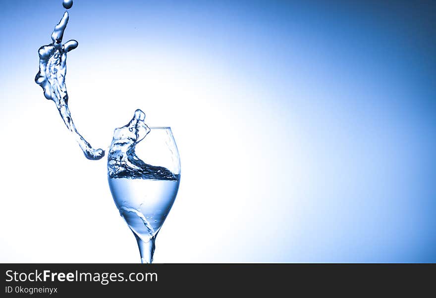 Water splashing out of falling glass on blue background with copy space.