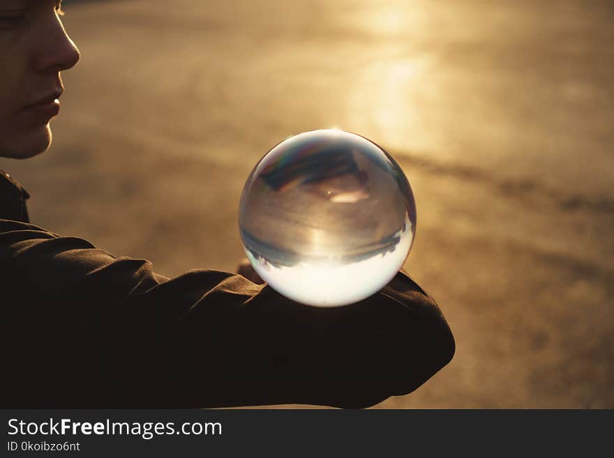 Contact juggling. Guy balances with glass ball on bent elbow. Inverted panorama of city in reflection of ball. Mastery of representation. Close-up photo at sunset.