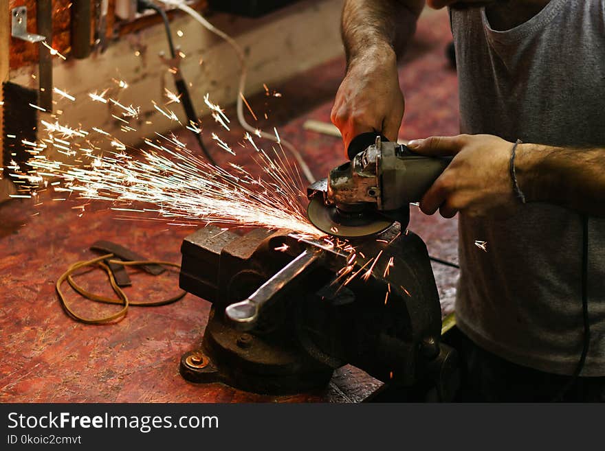 Blacksmith polishes crossguard of sword. Man is working in workshop. He holds a grinder in his hands.