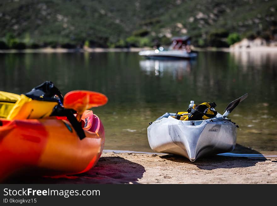 A pair of Kayaks beached on the shore of a lake in the summer time