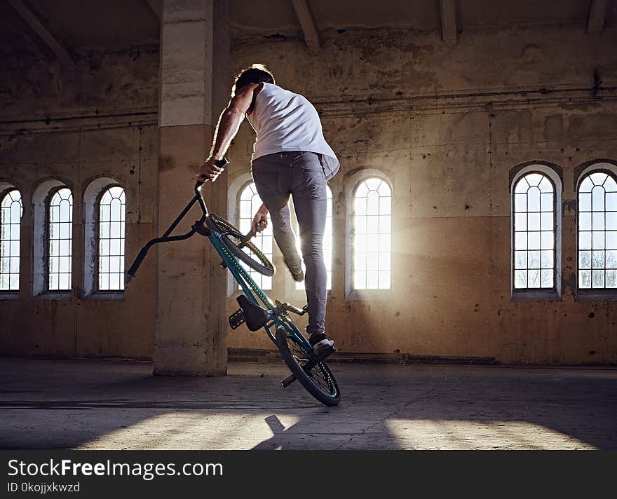 BMX stunt and jump riding in a hall with sunlight.