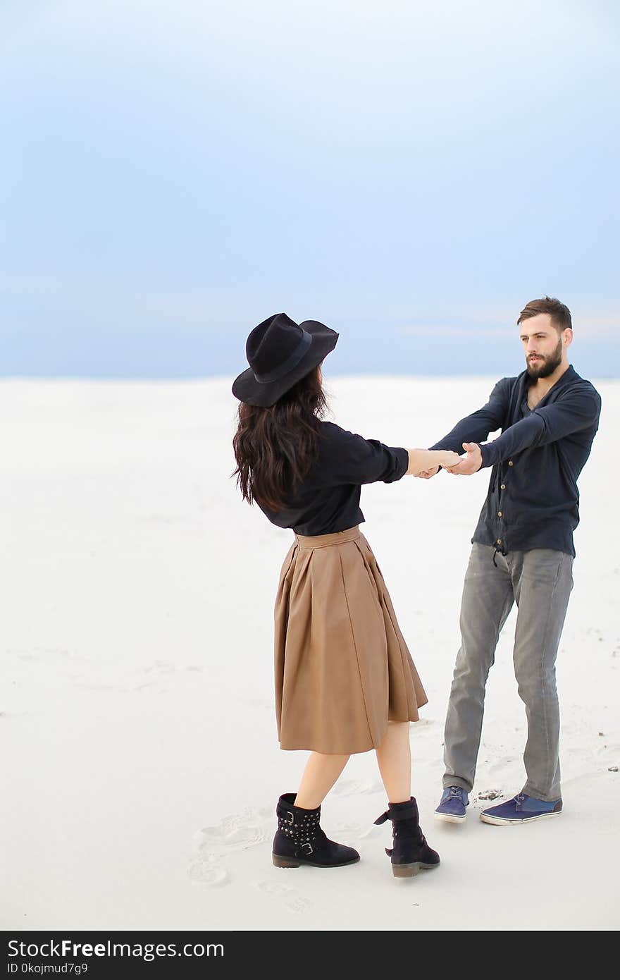 Young Woman Wearing Skirt Nad Hat Holding Hands Of Handsome Man On Snow In White Background.